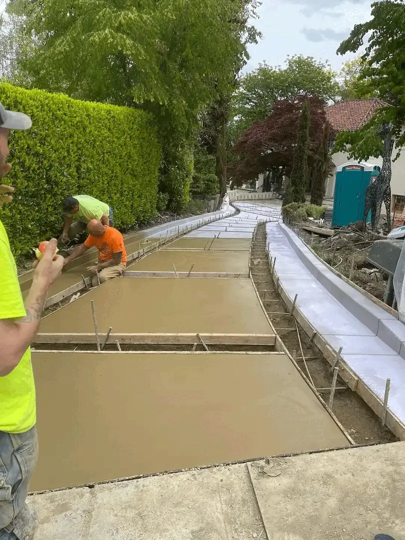 Workers pouring and finishing tan-colored concrete for a custom driveway installation in Seattle.