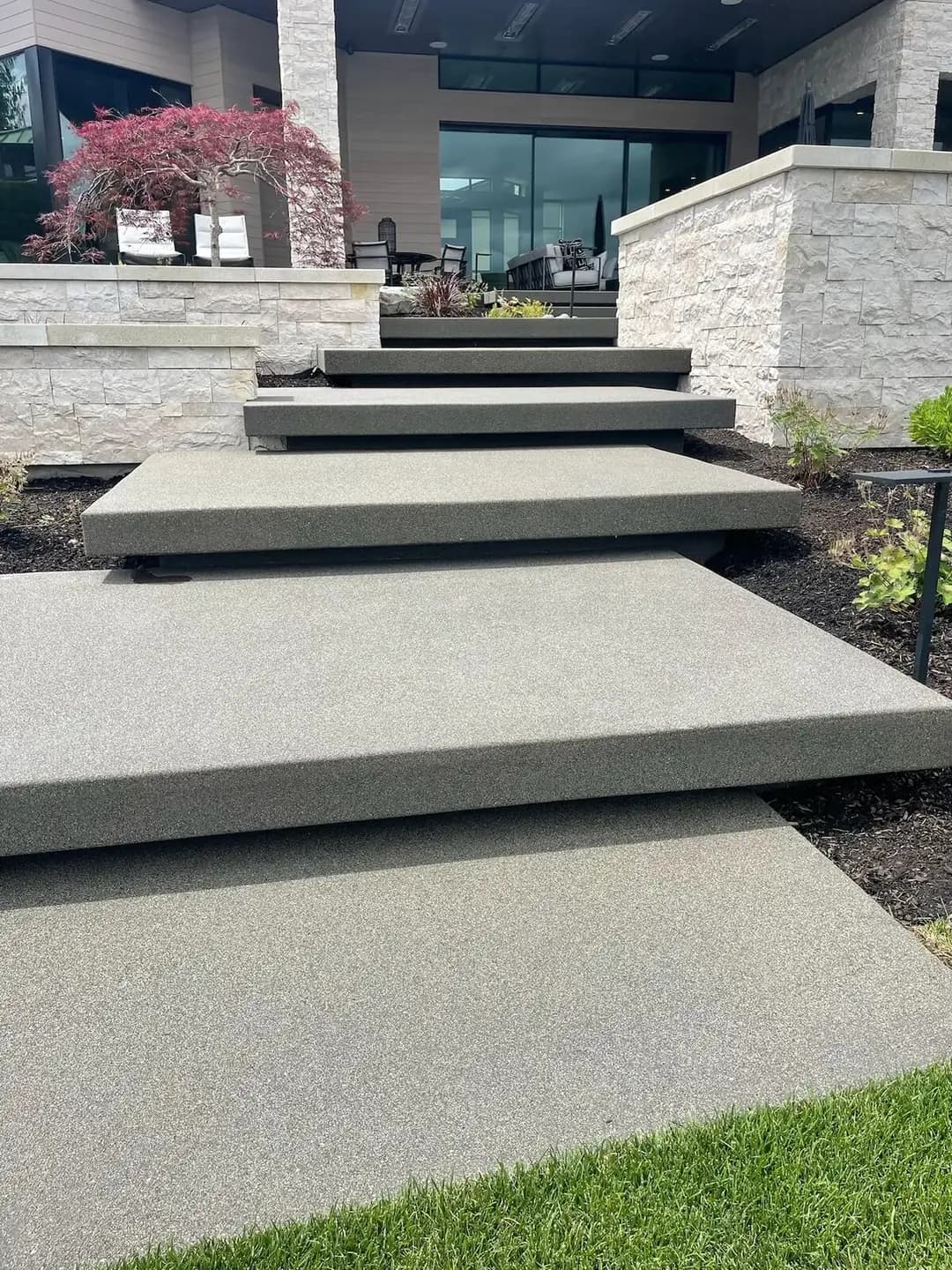 Front view of a wide floating concrete staircase ascending a landscaped slope towards a modern residence.
