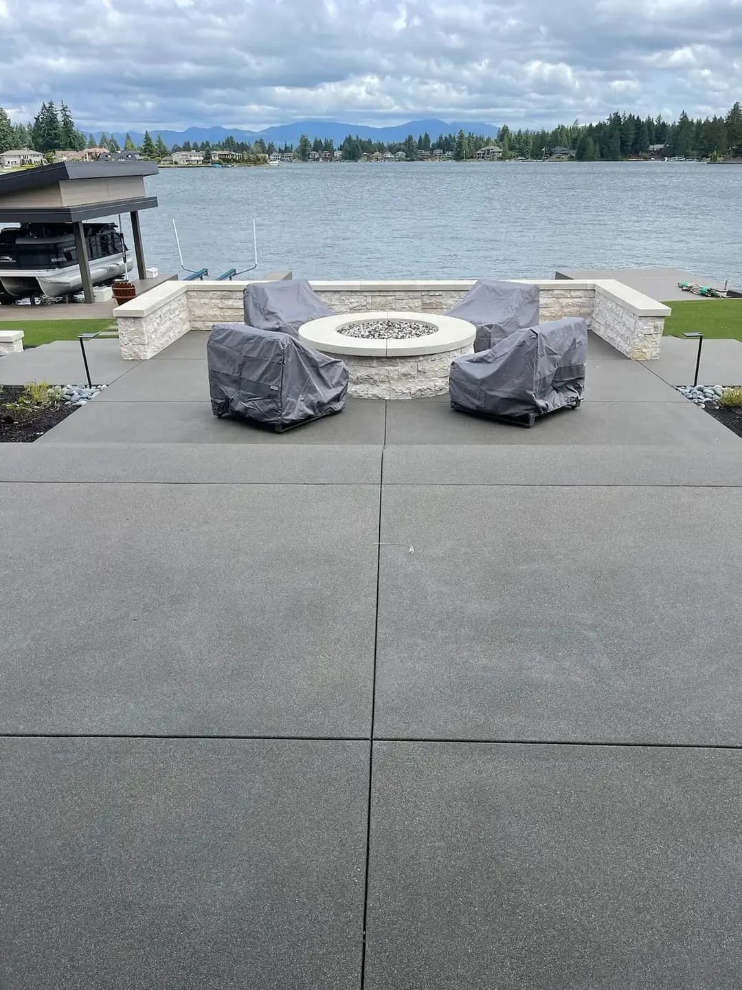 Overhead view of the charcoal exposed aggregate patio centered around a stone fire pit with covered chairs.