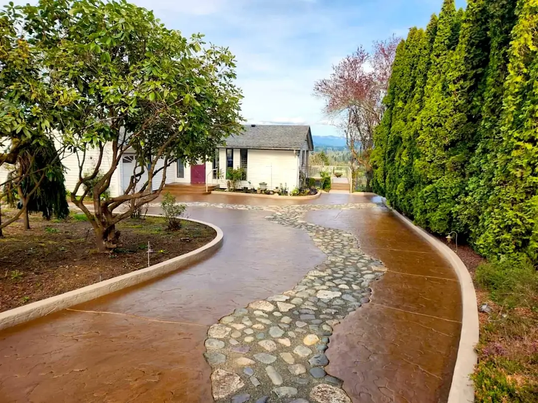 A finished stamped concrete driveway in Puyallup with a central path of inset river stones curving toward a house.
