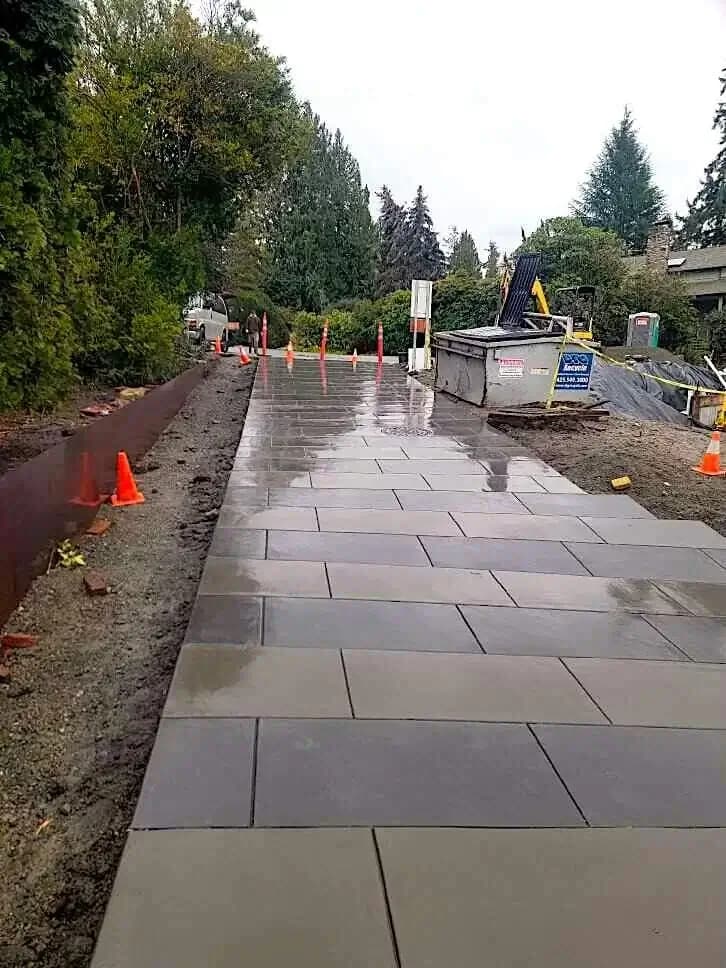 Long view of a new, wet concrete driveway with a large rectangular pattern in Yarrow Point, WA, lined with steel edging.