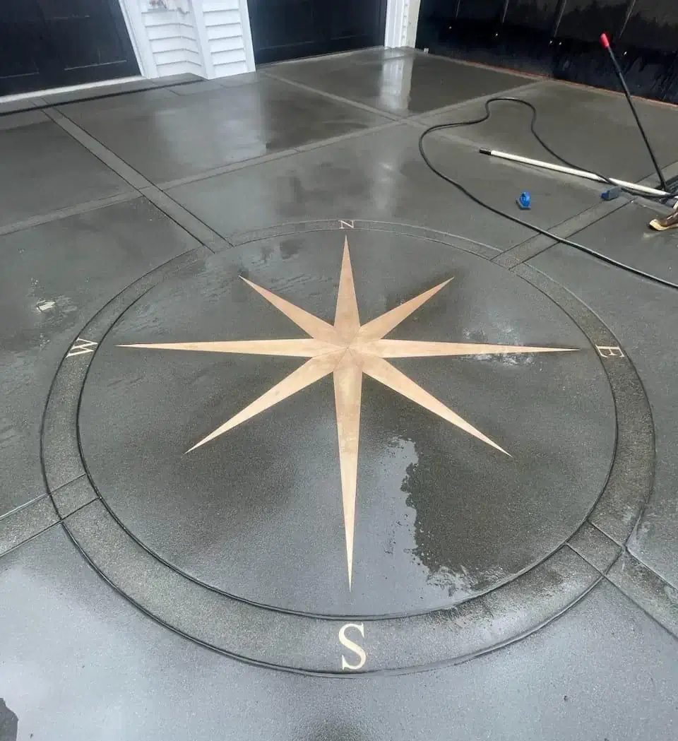 Finished custom concrete driveway in Bellevue with a detailed, stained compass rose inlay and dark gray pads.