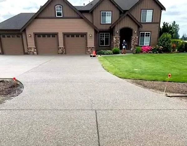 Wide view of a new exposed aggregate concrete driveway in Alderton, WA, leading to a three-car garage.