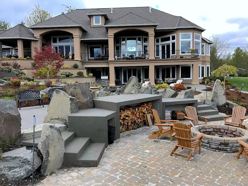 Custom concrete patio seating and firewood storage integrated with large boulders in Puyallup, WA.