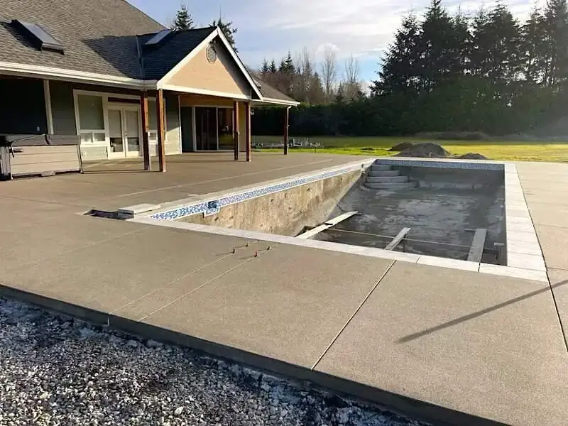 Wide view of a new sand finish concrete pool deck and patio recently installed at a home in Puyallup, Washington.