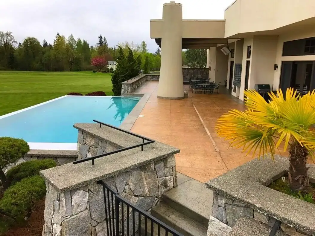 Wide view of a stamped concrete pool deck and patio at a modern home in Bellevue with an infinity pool.