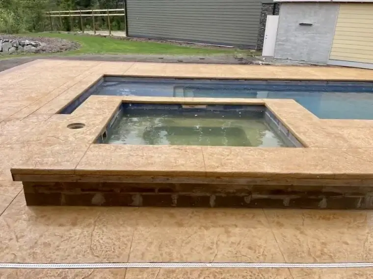 Overview of a stamped concrete pool deck and hot tub surround in Puyallup, showing the warm sandstone color.