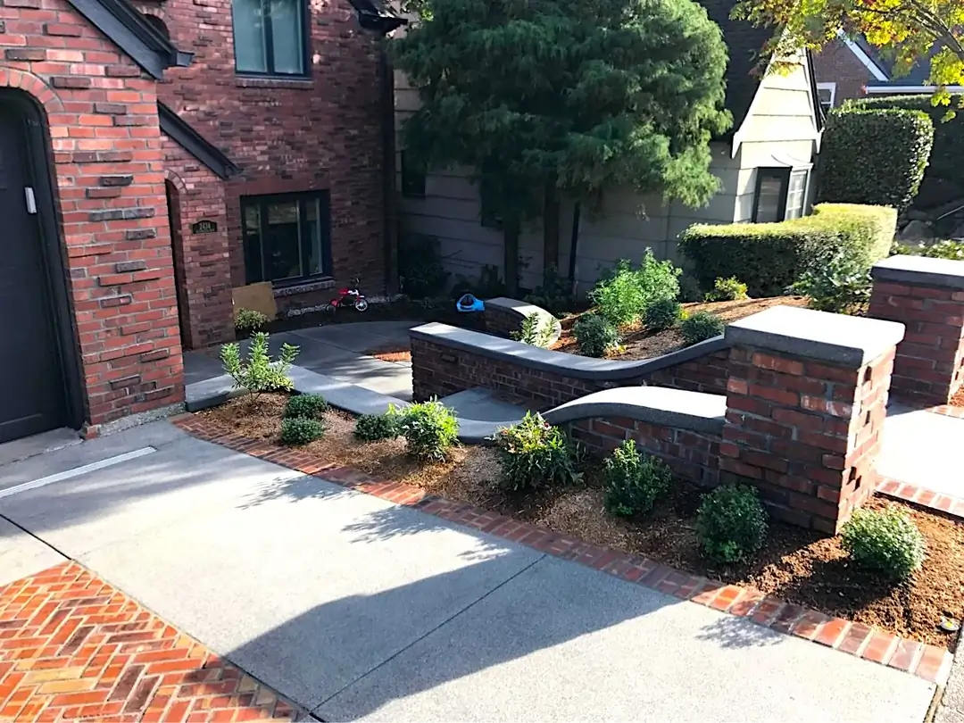 Broomed concrete walkway with a red stamped brick border leading to curved retaining walls in Tacoma, Washington.