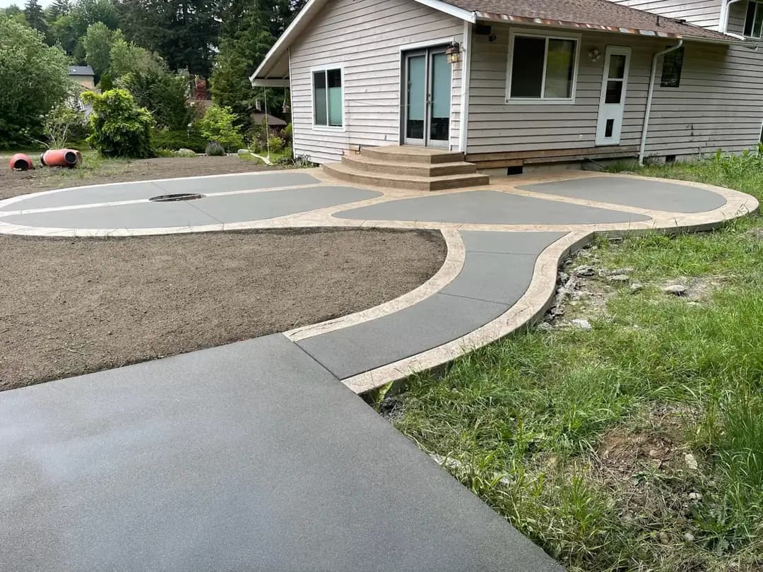 A modern two-tone concrete patio and walkway installation in Puyallup with curved, organic shapes and a sand finish.